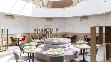 A modern hotel lobby with round tables, cushioned seating, and a central decorative structure.