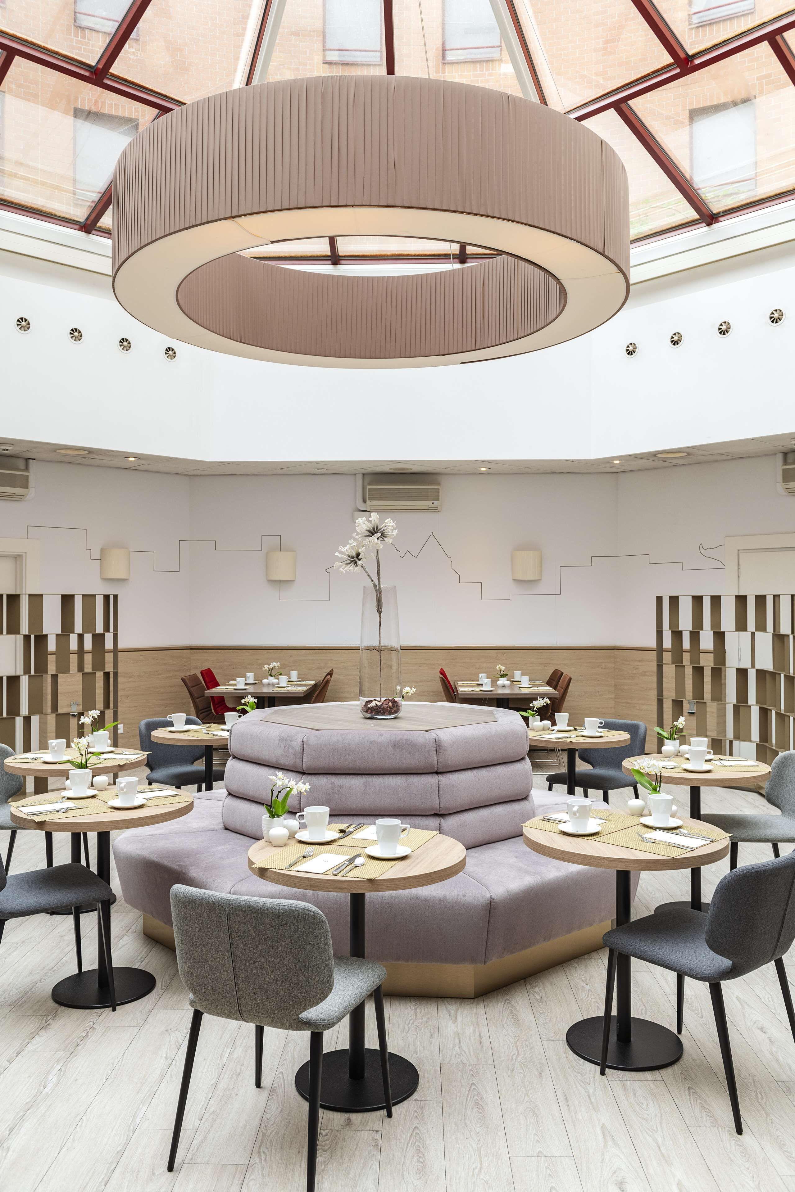 A modern interior with a central seating area, round tables, and a high ceiling with skylights.