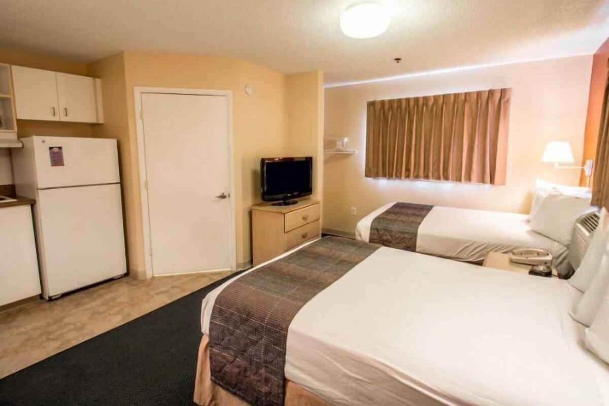 A hotel room with two beds, a television, a refrigerator, and a small desk.