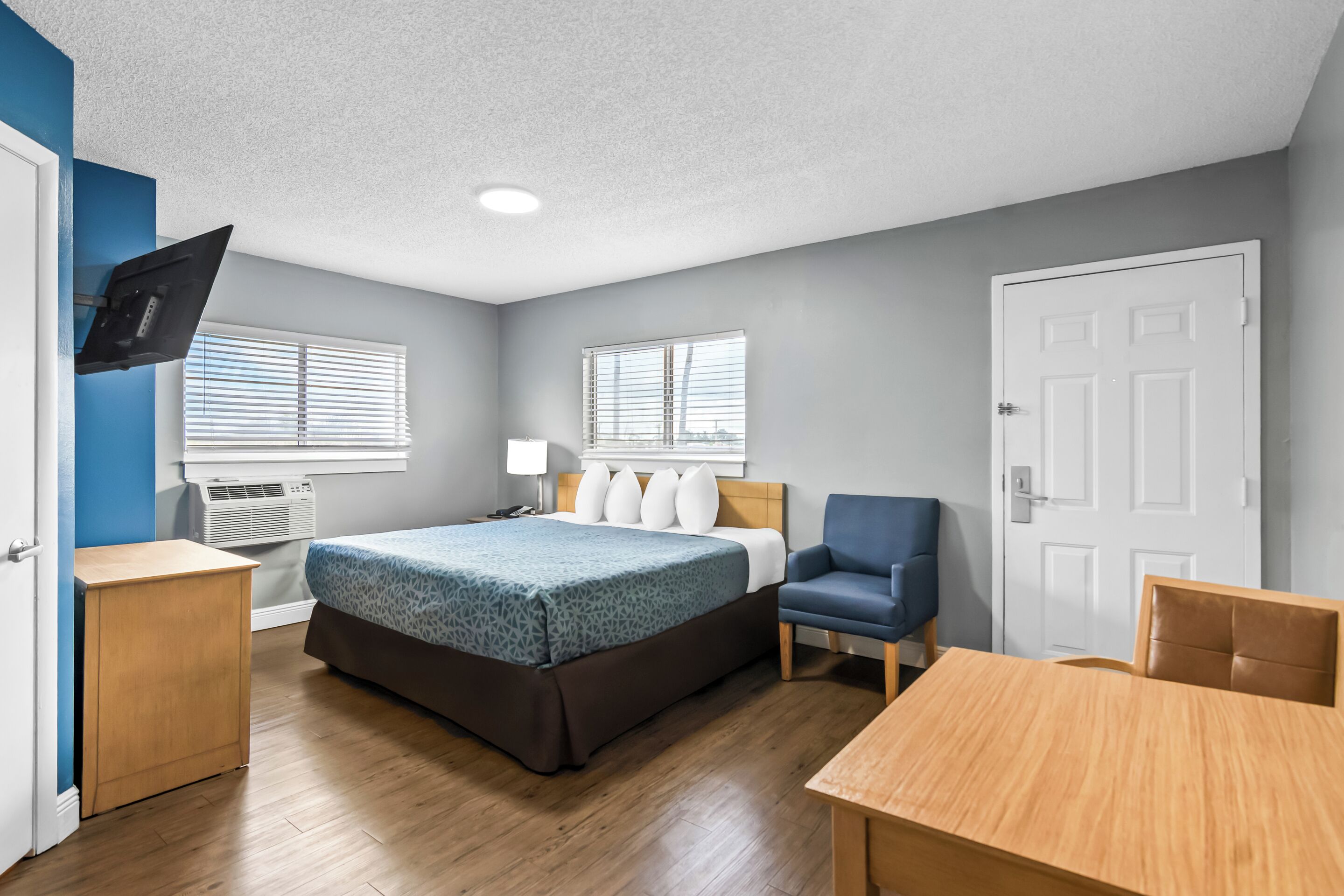A hotel room with a bed, a desk, a chair, and a TV mounted on the wall.