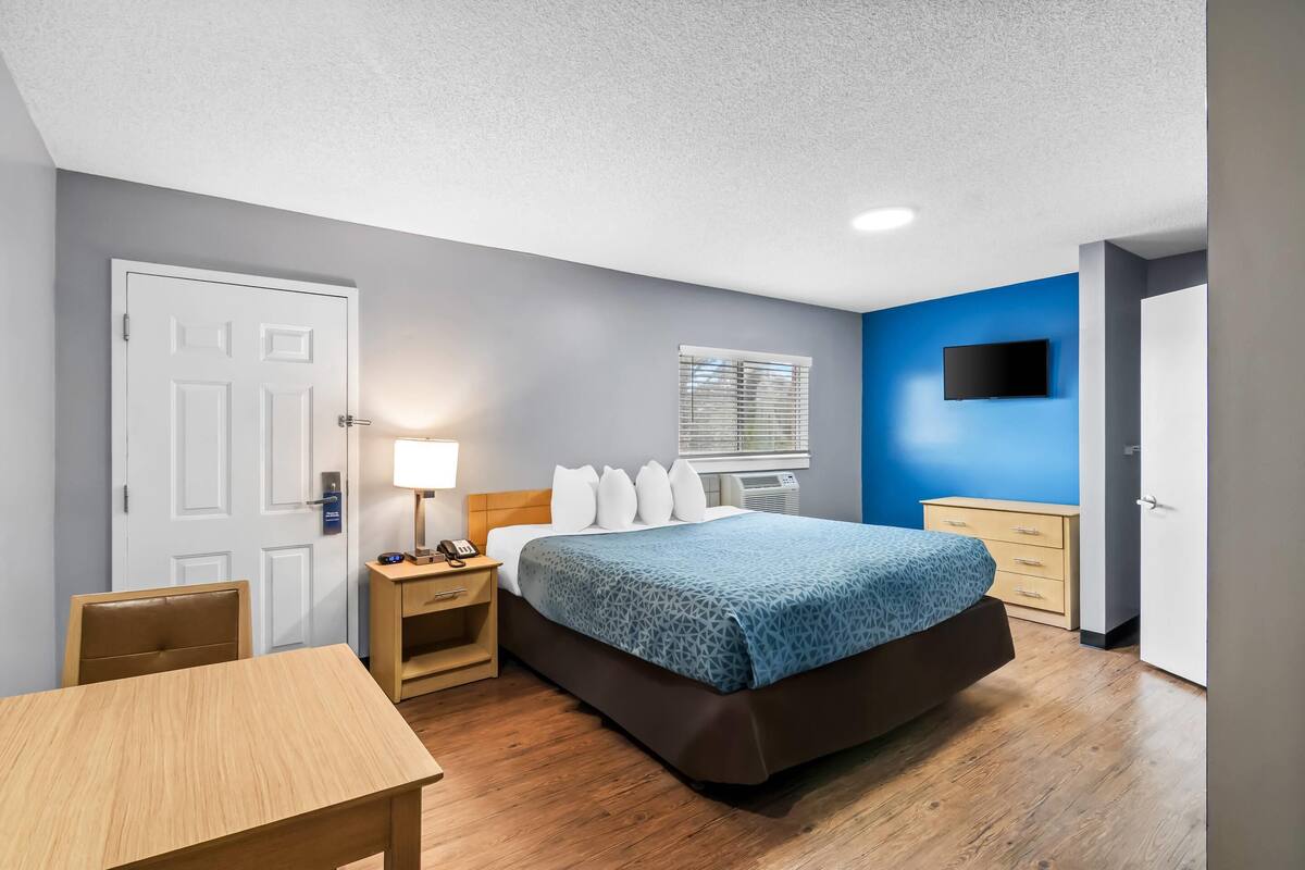 A bedroom with a bed, bedside table, lamp, and a TV mounted on the wall.