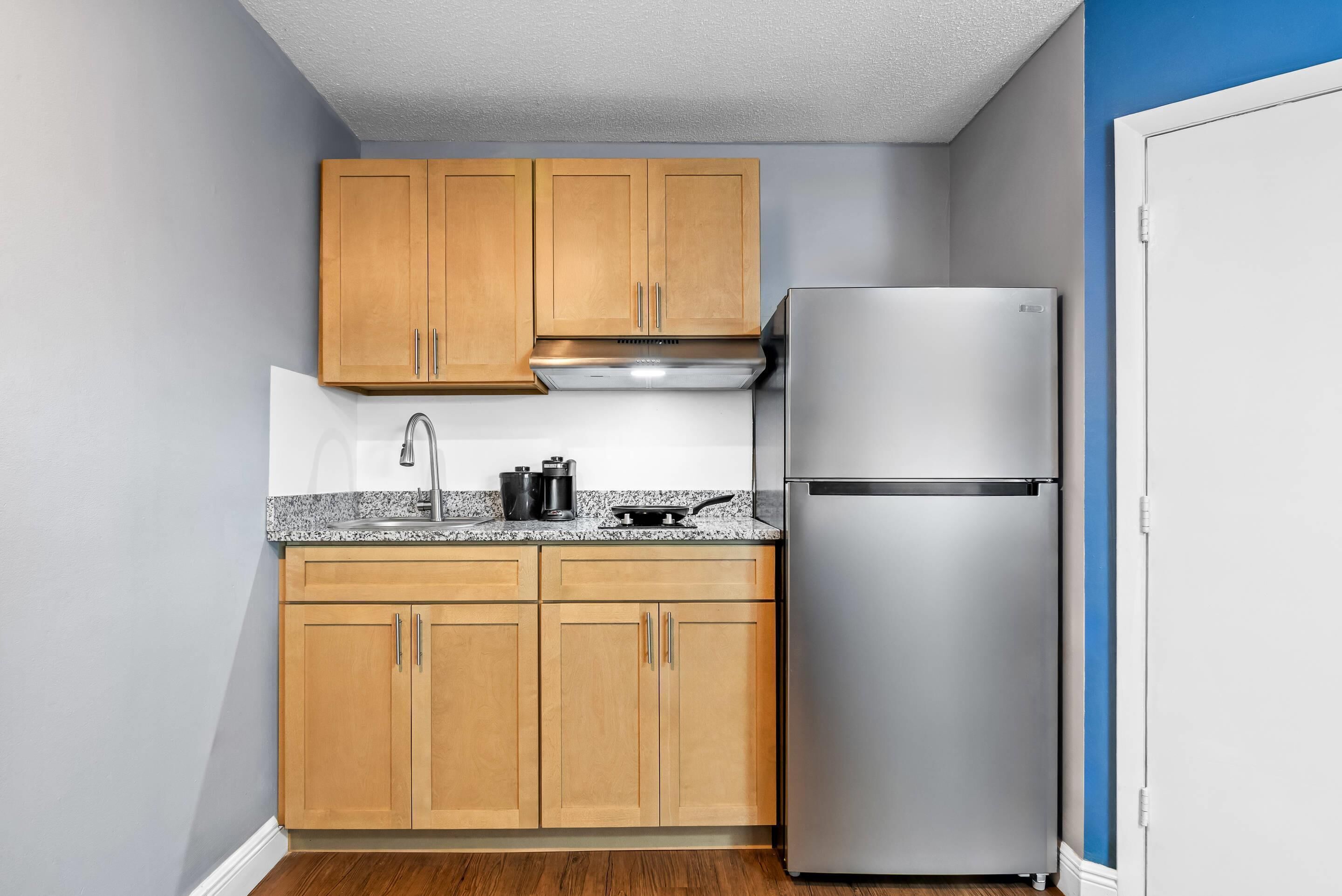 Una cocina compacta con armarios de madera, un refrigerador de acero inoxidable y una encimera de granito.