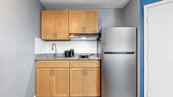 Una cocina compacta con armarios de madera, un refrigerador de acero inoxidable y una encimera de granito.