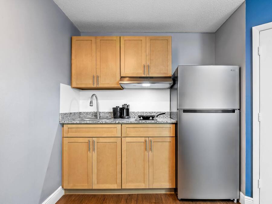 A compact kitchen with wooden cabinets, a stainless steel refrigerator, and a granite countertop.