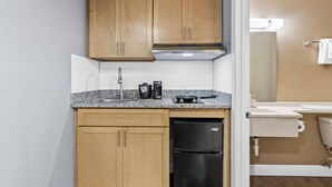 Una cocina compacta con armarios de madera, una campana extractora de acero inoxidable, un refrigerador negro y una encimera de granito.