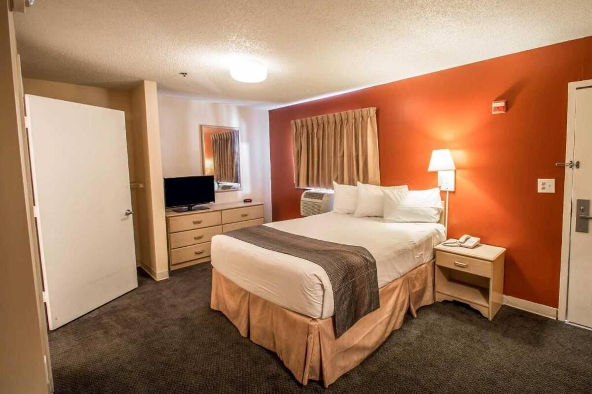 A hotel room with a bed, bedside table, lamp, TV, and a wardrobe.