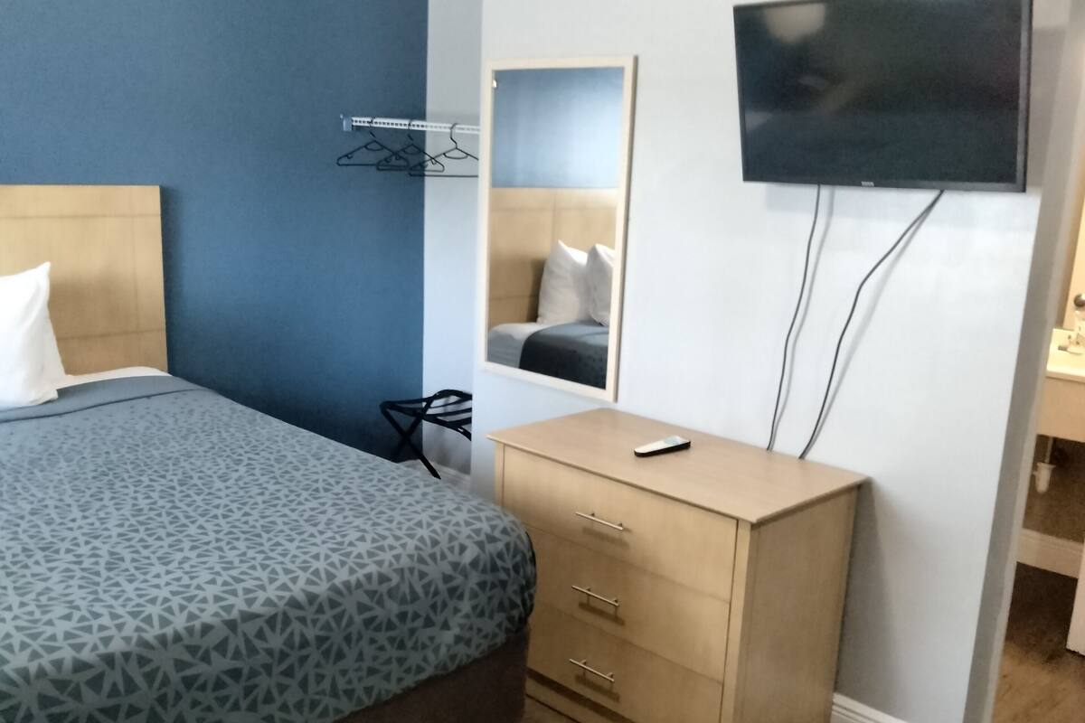 A hotel room with a bed, a dresser, a mirror, and a TV mounted on the wall.