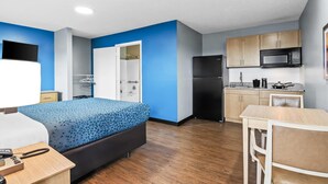 Habitación de hotel pequeña con cama, mesita de noche y zona de kitchenette que incluye microondas y refrigerador.