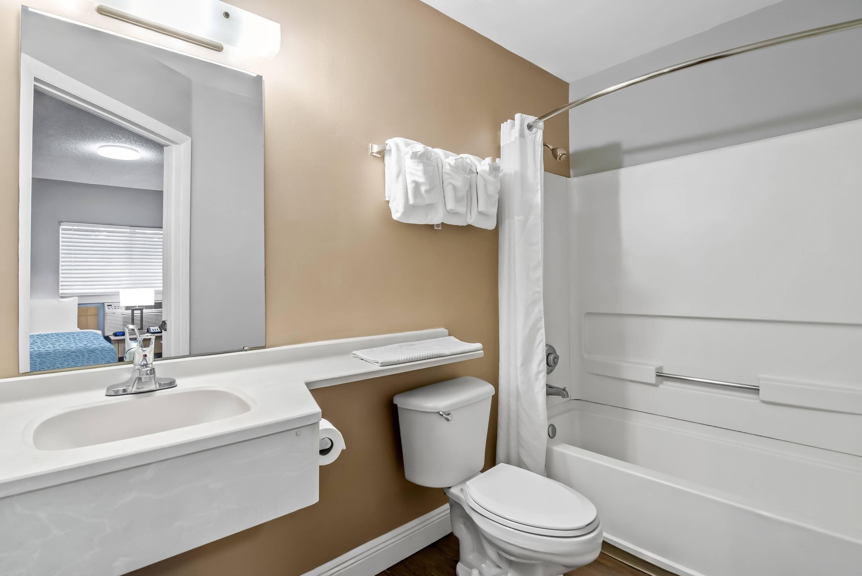 Un baño moderno con pared beige, sanitarios blancos, un lavabo, inodoro y una ducha con cortina.