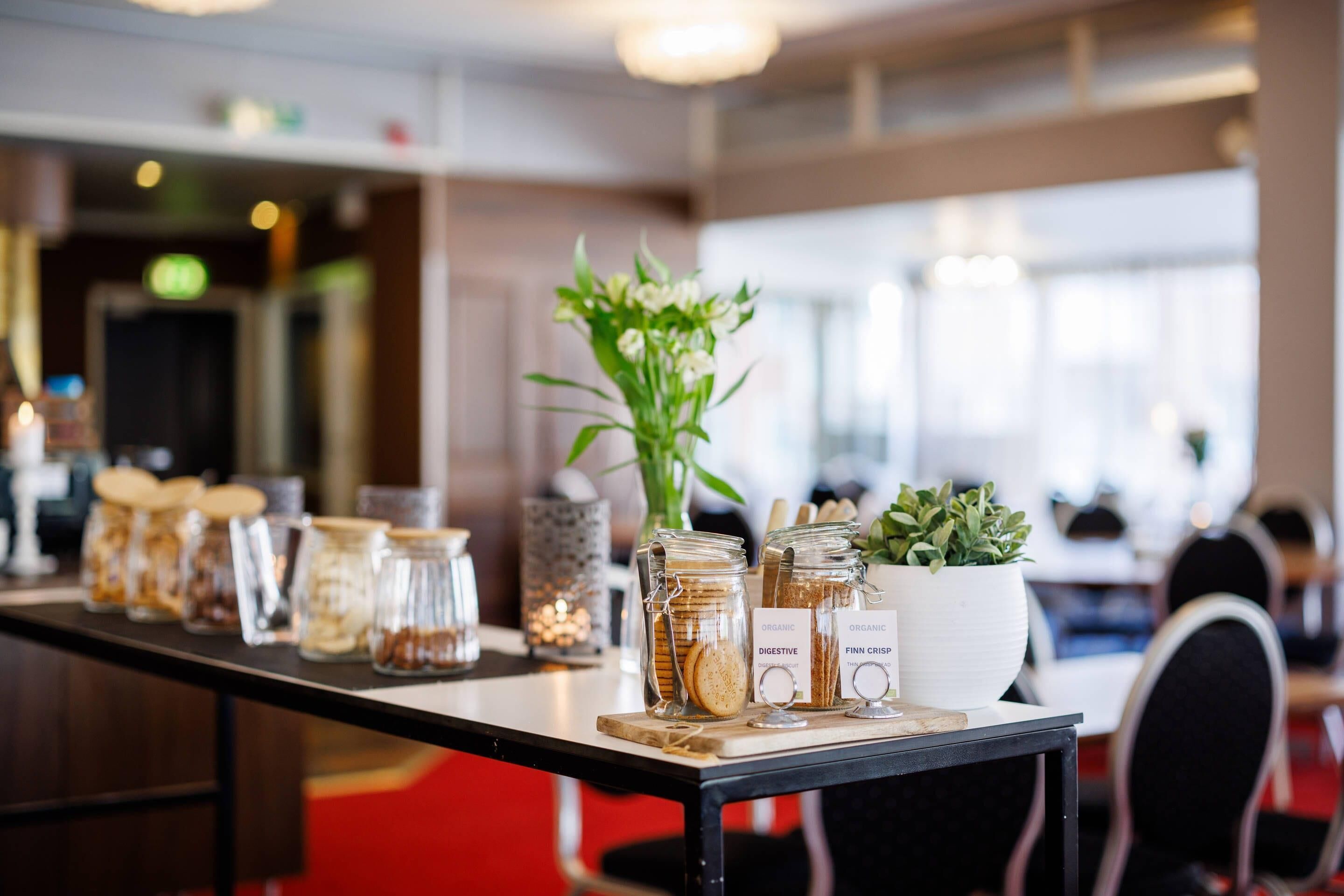 A long table with jars of snacks, a potted plant, and a sign indicating organic and digestible options.