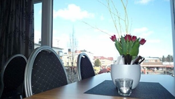 A dining table with a vase of red tulips, a glass of water, and a view of buildings through a window. - Quality Hotel Bodensia (Boden)