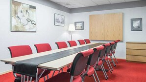 A conference room with a long table and red chairs, white walls, and framed artwork. - Quality Hotel Bodensia (Boden)
