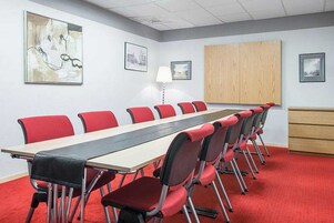 Un salón de conferencias con una larga mesa y sillas rojas, paredes blancas y cuadros enmarcados.