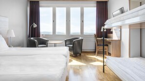 A hotel room with two beds, a desk, a chair, a lamp, and a view of the mountains through large windows. - Quality Hotel Bodensia (Boden)