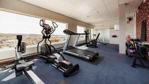 A gym with treadmills, stationary bikes, and a rowing machine, with a view of a cityscape through large windows. - Quality Hotel Bodensia (Boden)