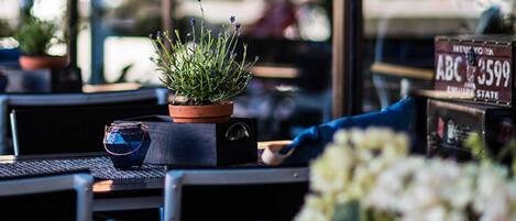 L’intérieur d’un restaurant, avec une plante en pot sur une table, un panneau indiquant un numéro de téléphone et une fenêtre reflétant l’extérieur.