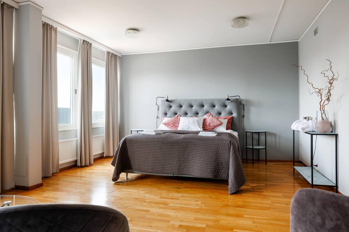 A bedroom with a large bed, a bedside table, a chair, and a view of the outdoors.