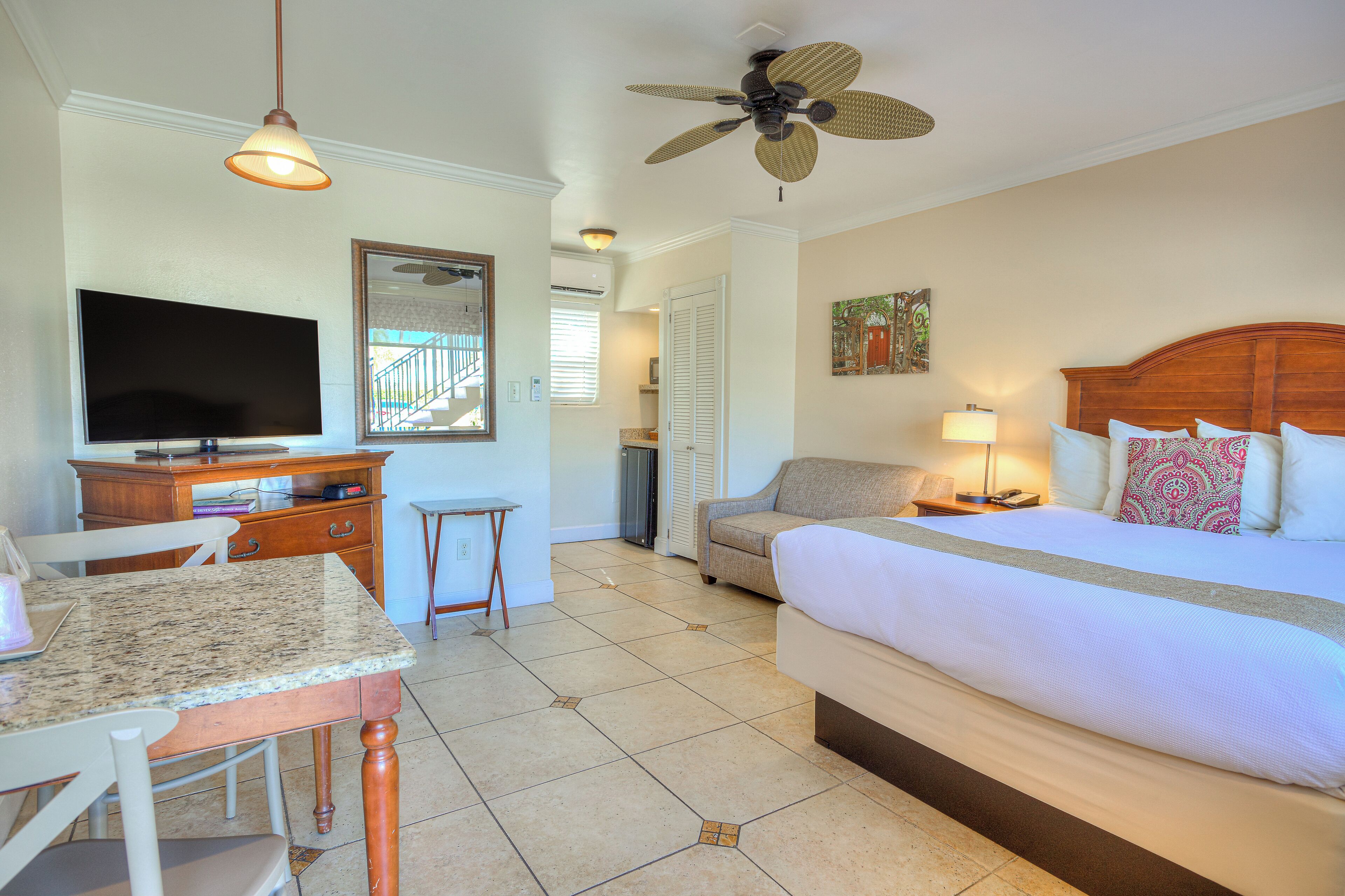 A hotel room with a bed, desk, TV, and a ceiling fan.