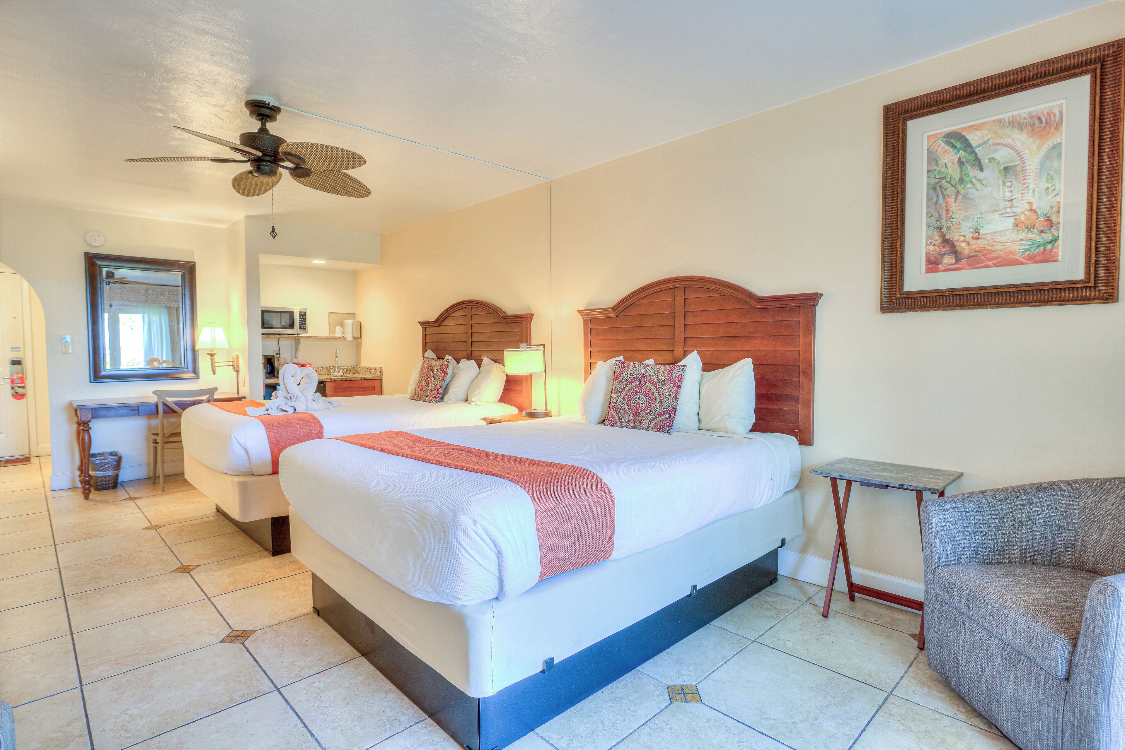 A hotel room with a large bed, a desk, a chair, and a ceiling fan.