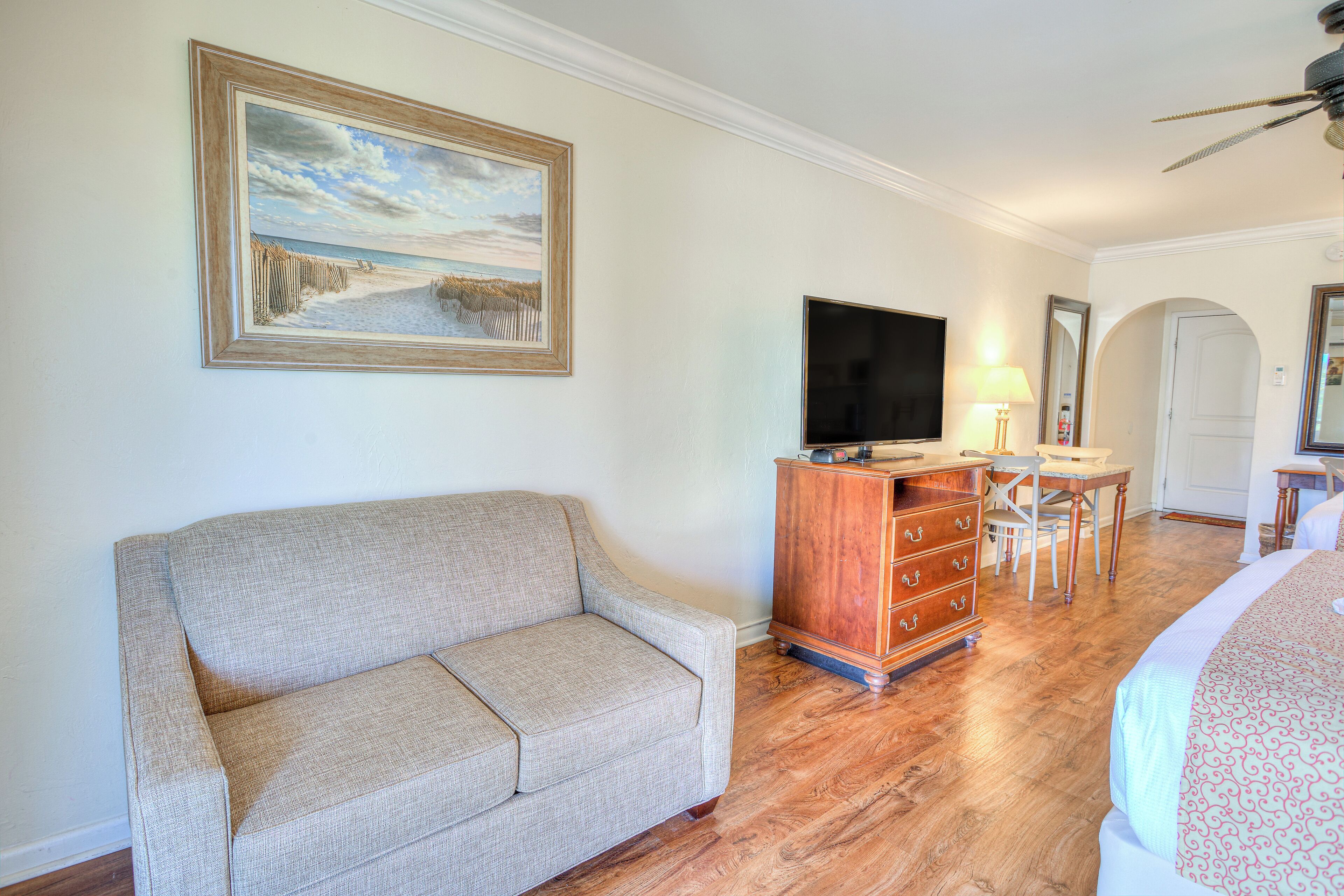 A hotel room with a sofa, a television, a desk with a chair, and a dresser.