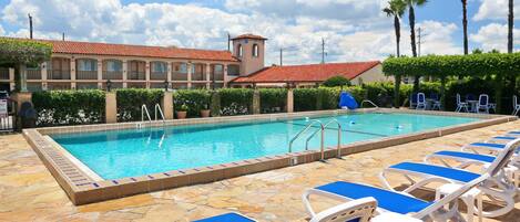 A swimming pool with lounge chairs and a building with a red-tiled roof.