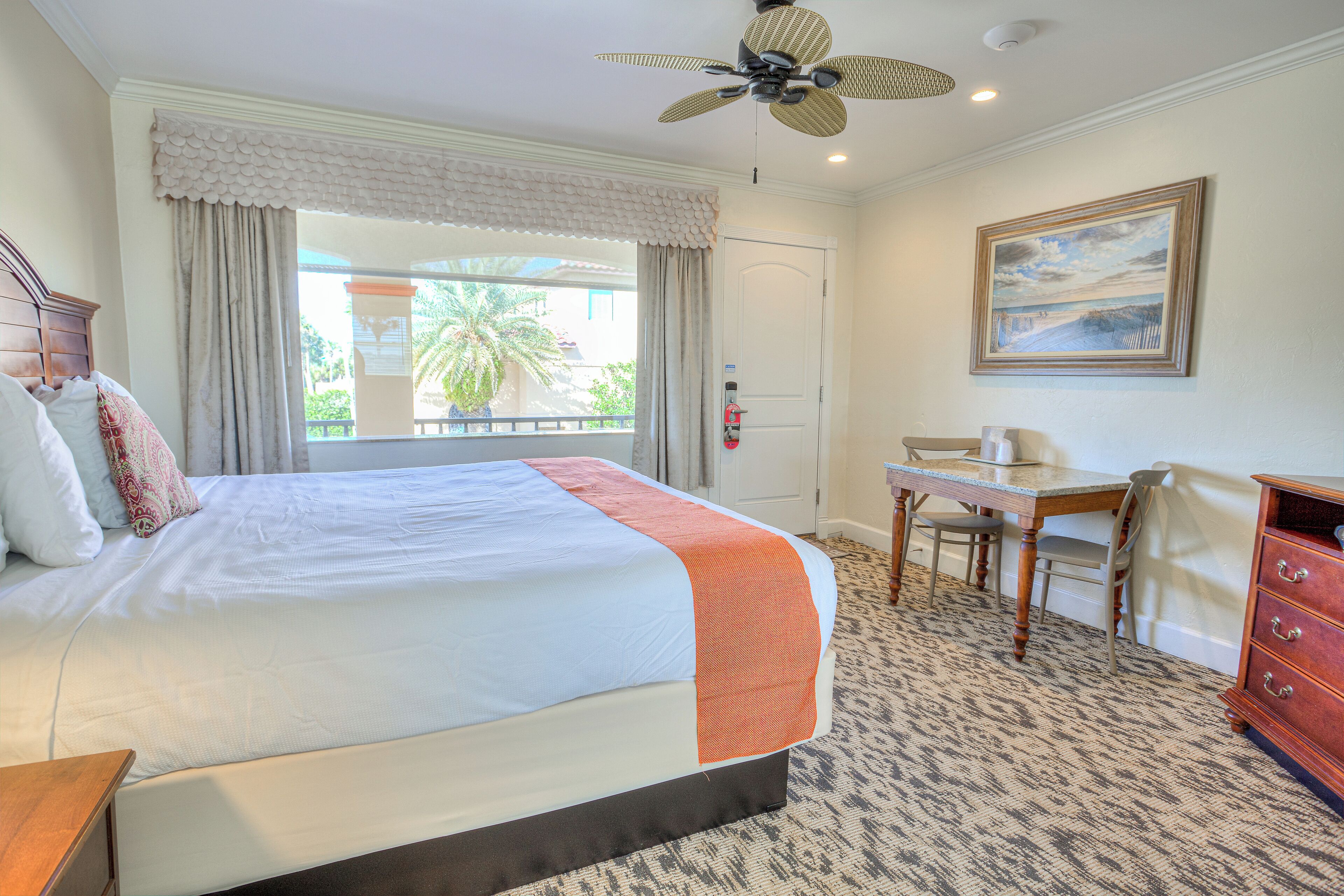 A hotel room with a bed, a desk, a chair, a dresser, and a ceiling fan.