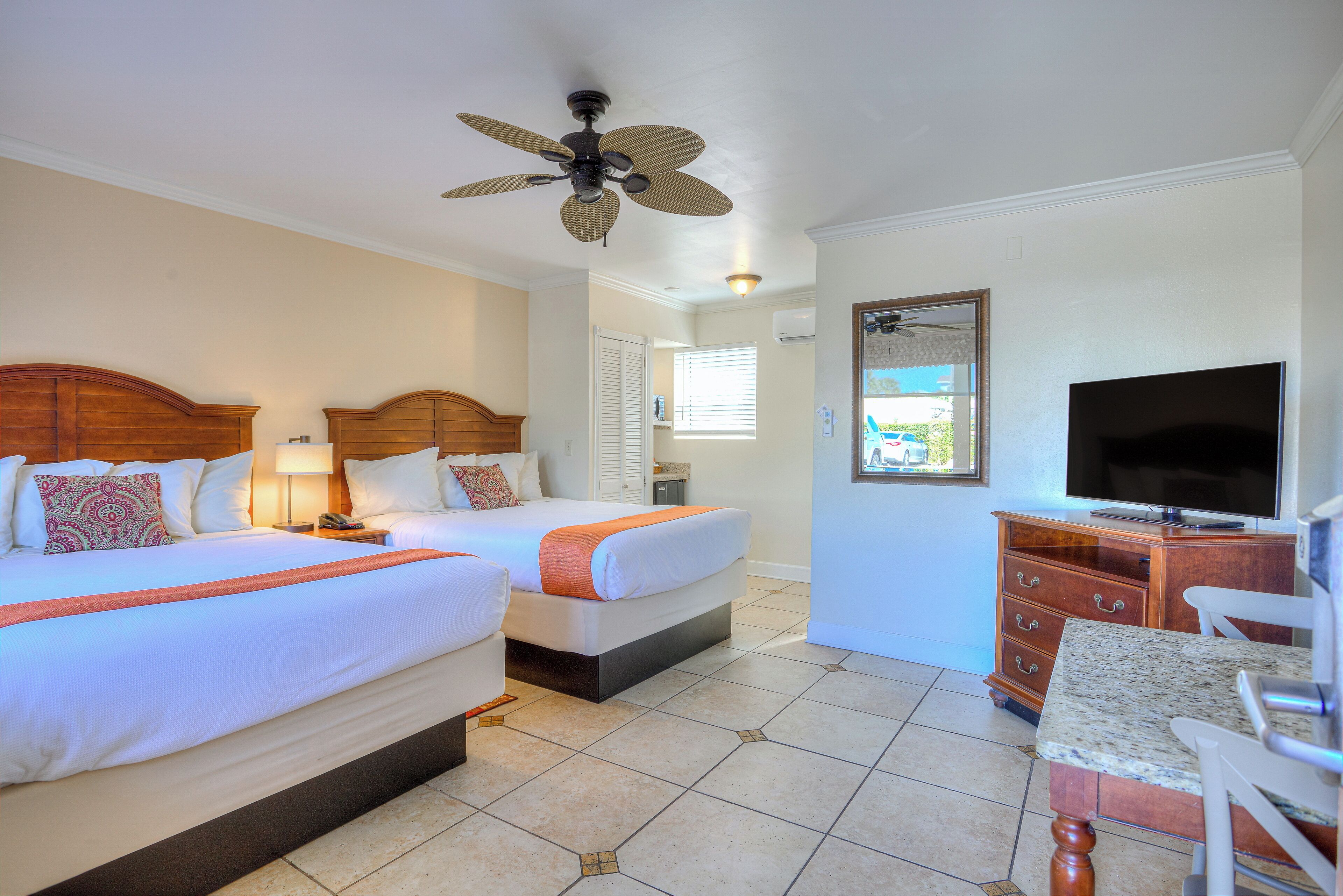 A hotel room with two beds, a ceiling fan, a TV, and a dining area with a table and chairs.