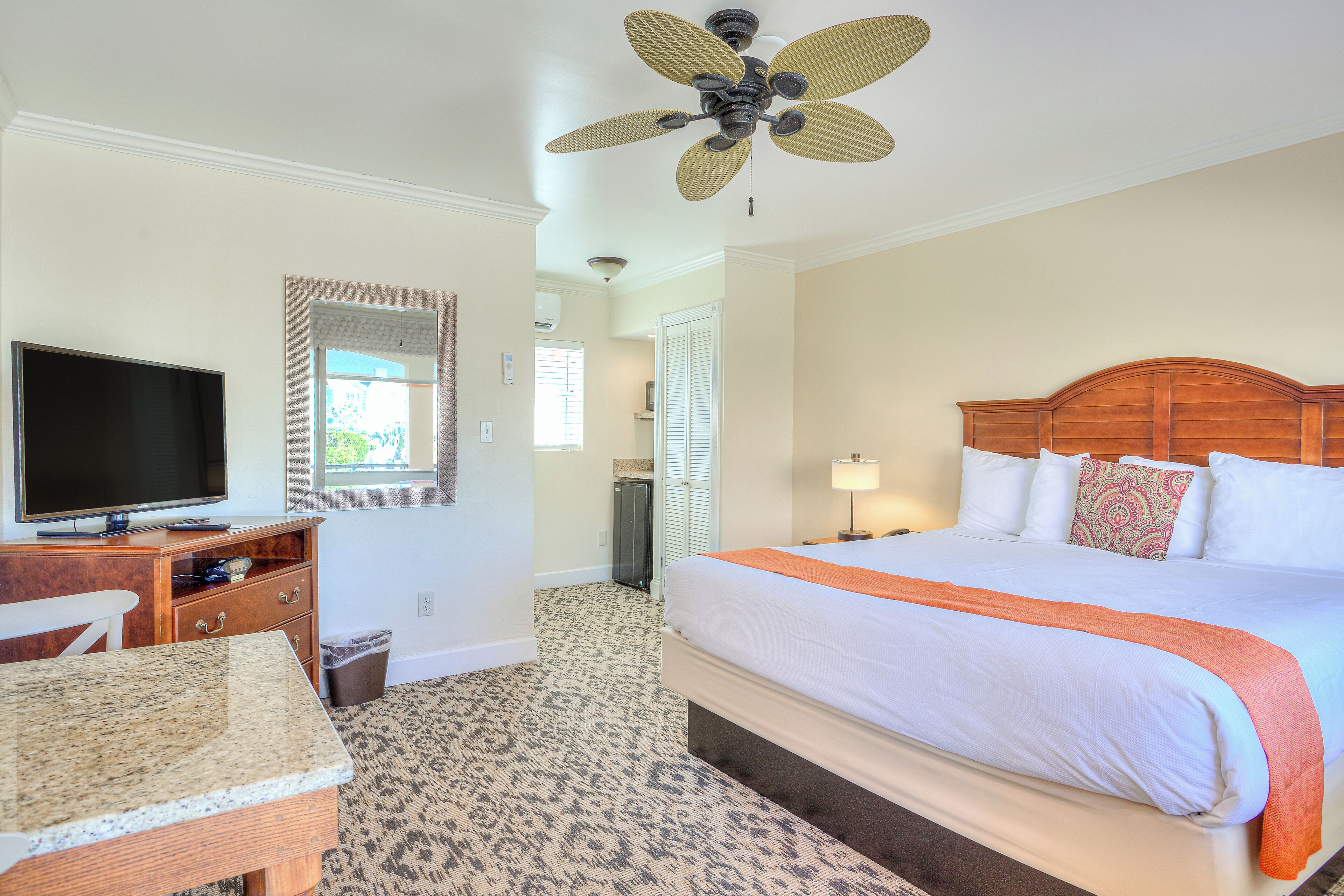 A hotel room with a bed, a television, a desk, and a ceiling fan.