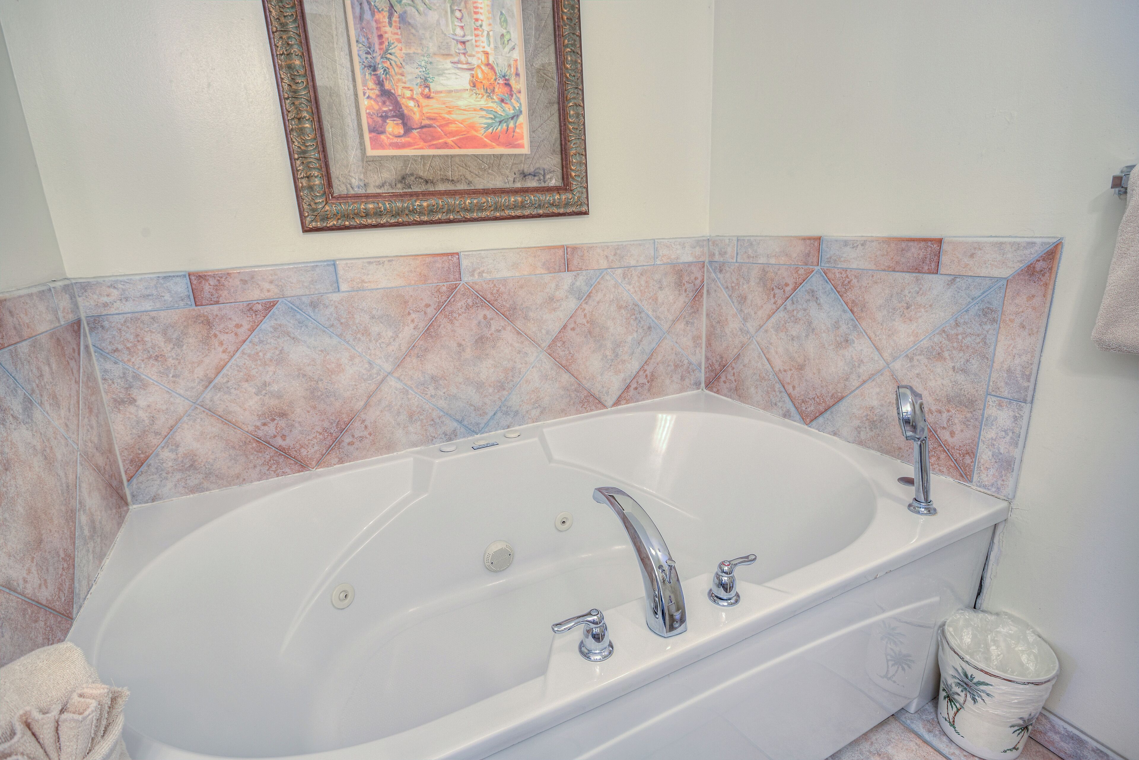 Eine große, weiße Badewanne mit zwei Wasserhähnen und einem Ablauf, vor einer gefliesten Wand mit geometrischem Muster.