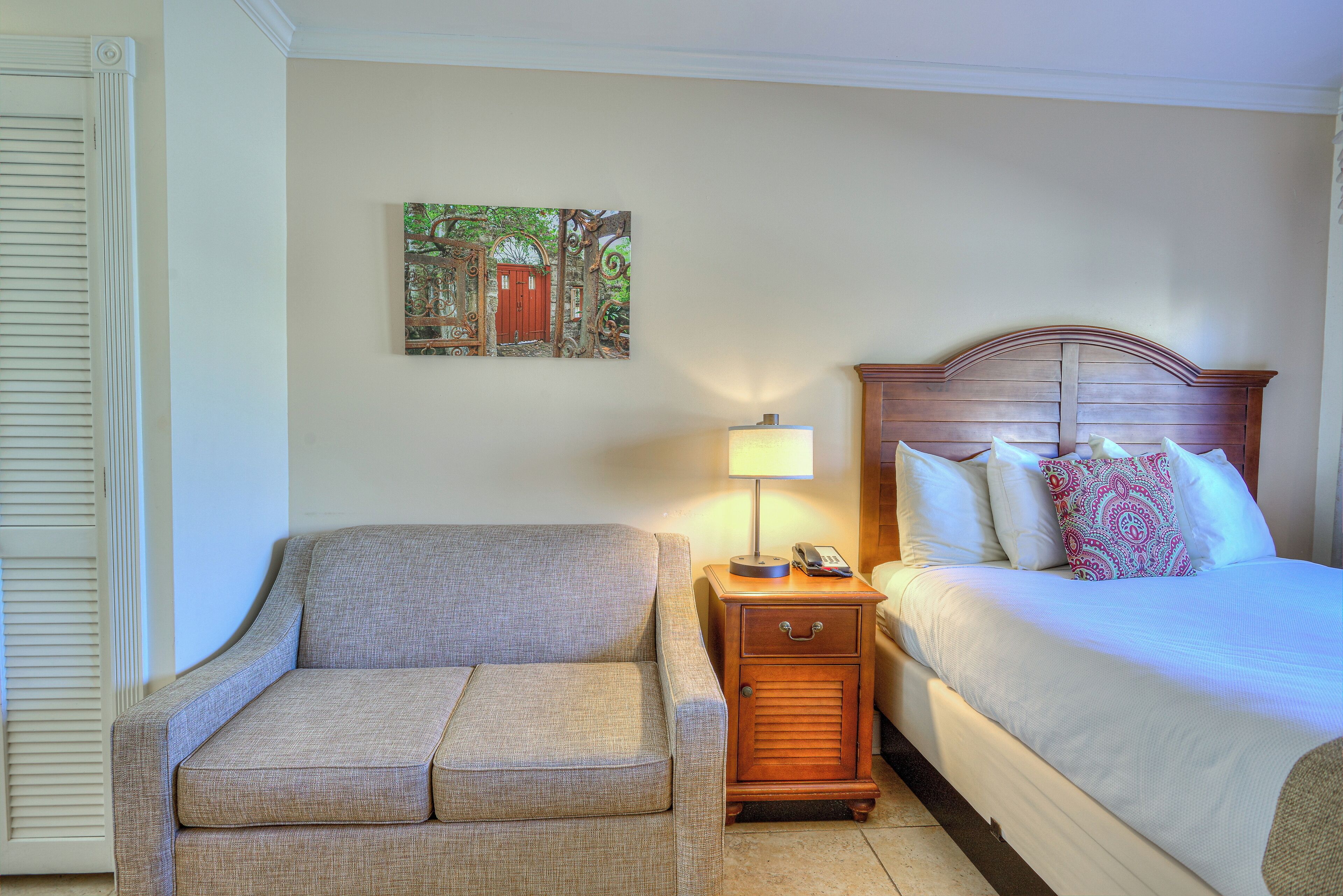 A bedroom with a bed, bedside table, lamp, and a painting on the wall.