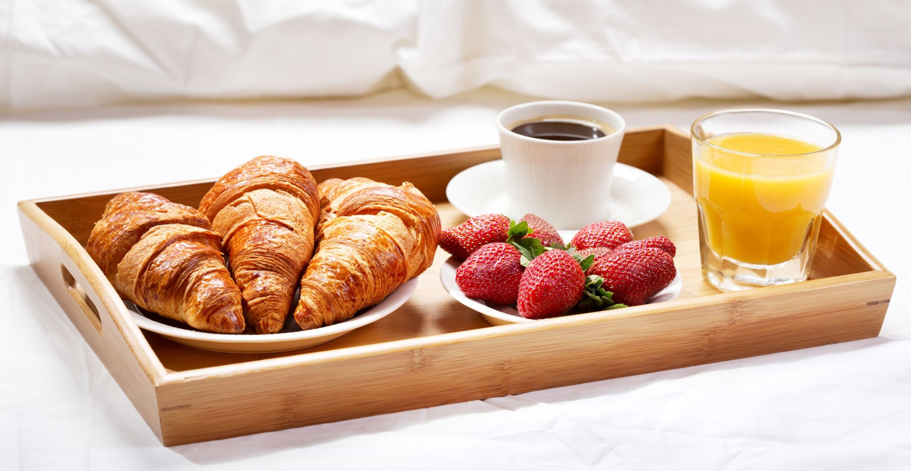Un plateau en bois avec des croissants, des fraises, une tasse de café et un verre de jus d’orange.