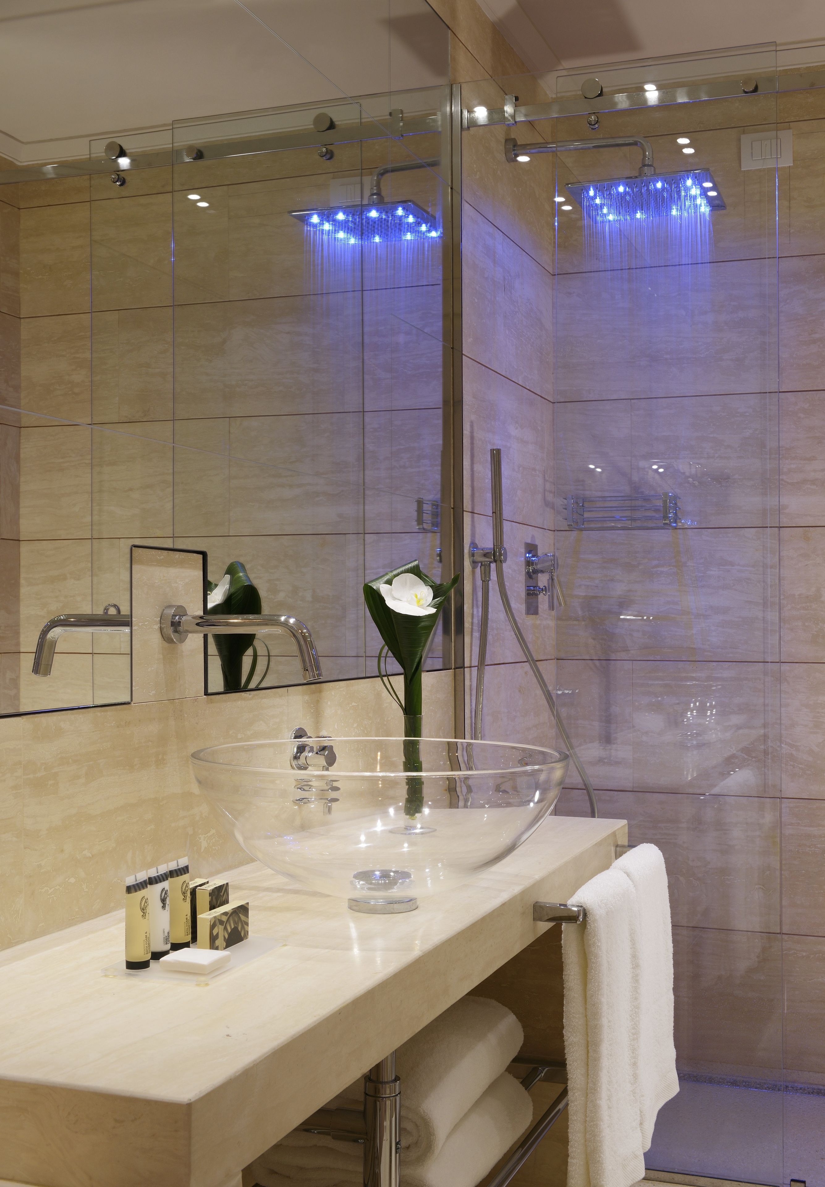 Ein modernes Badezimmer mit Duschkabine aus Glas, einem Waschtisch mit Glasbecken und einem Handtuchhalter.