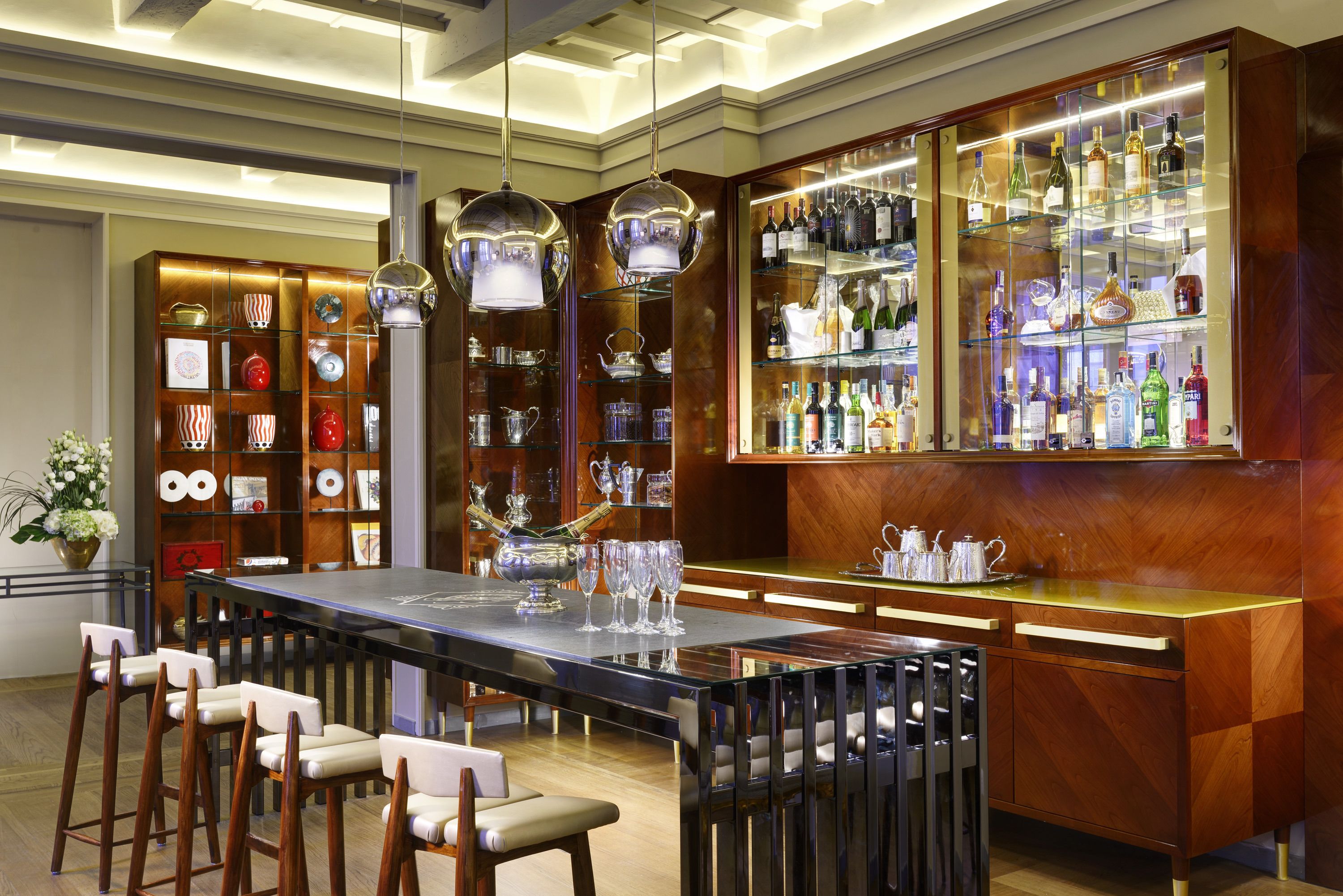 A modern bar area with a long counter, bar stools, and a display of liquor bottles.