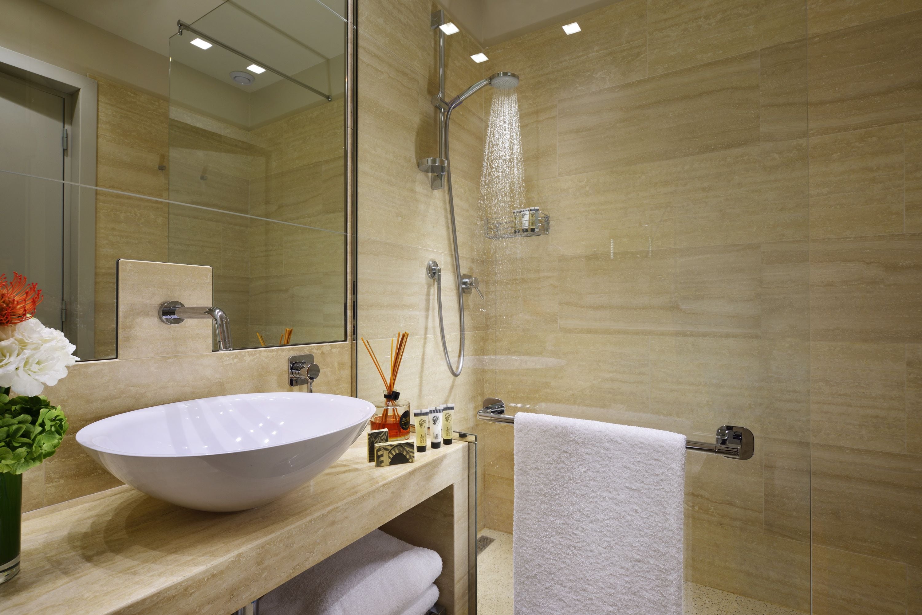 Un baño moderno con un lavamanos grande de color blanco, una ducha con cerramiento de vidrio y un espejo sobre el lavamanos.
