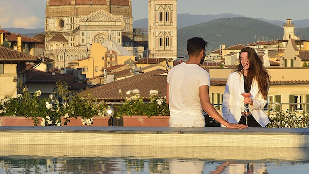 Una pareja junto a una piscina con vista a un edificio histórico.