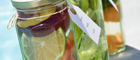Three glass jars with metal lids containing various fruits and herbs, placed on a ledge by a pool.