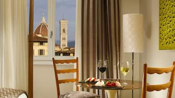 Habitación de hotel con una mesa de comedor preparada para dos personas, con vistas a un edificio histórico y una lámpara.