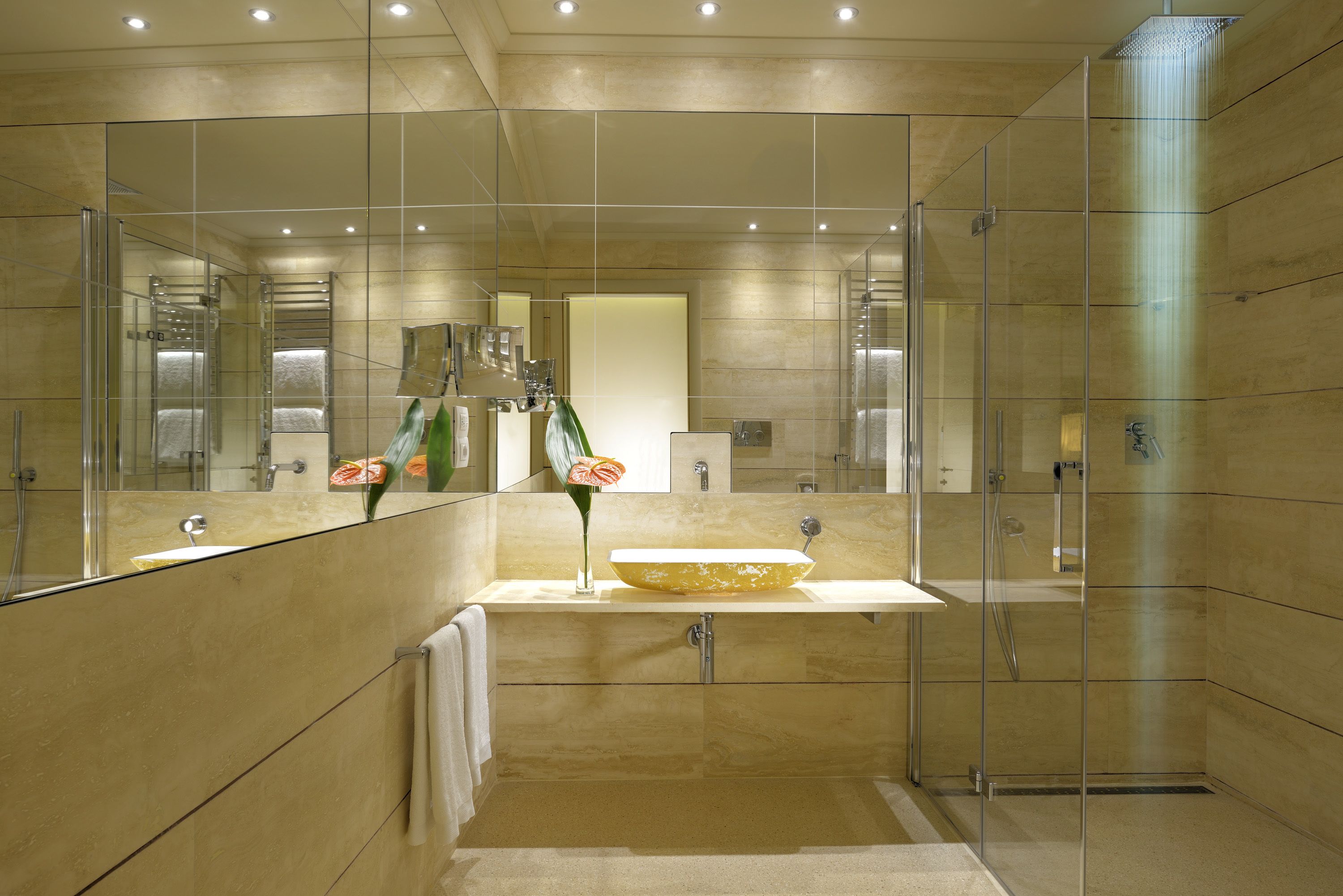 Une salle de bain moderne avec une douche à l’italienne en verre, un grand miroir et un mur recouvert de carreaux beiges.