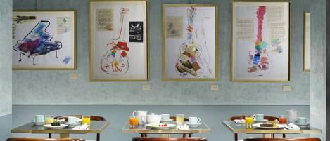 A dining area with tables set for breakfast, featuring artwork on the walls.