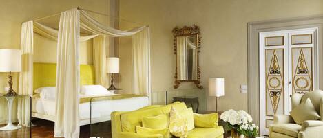 A luxurious room with a four-poster bed, a chandelier, a yellow sofa, and a large mirror.