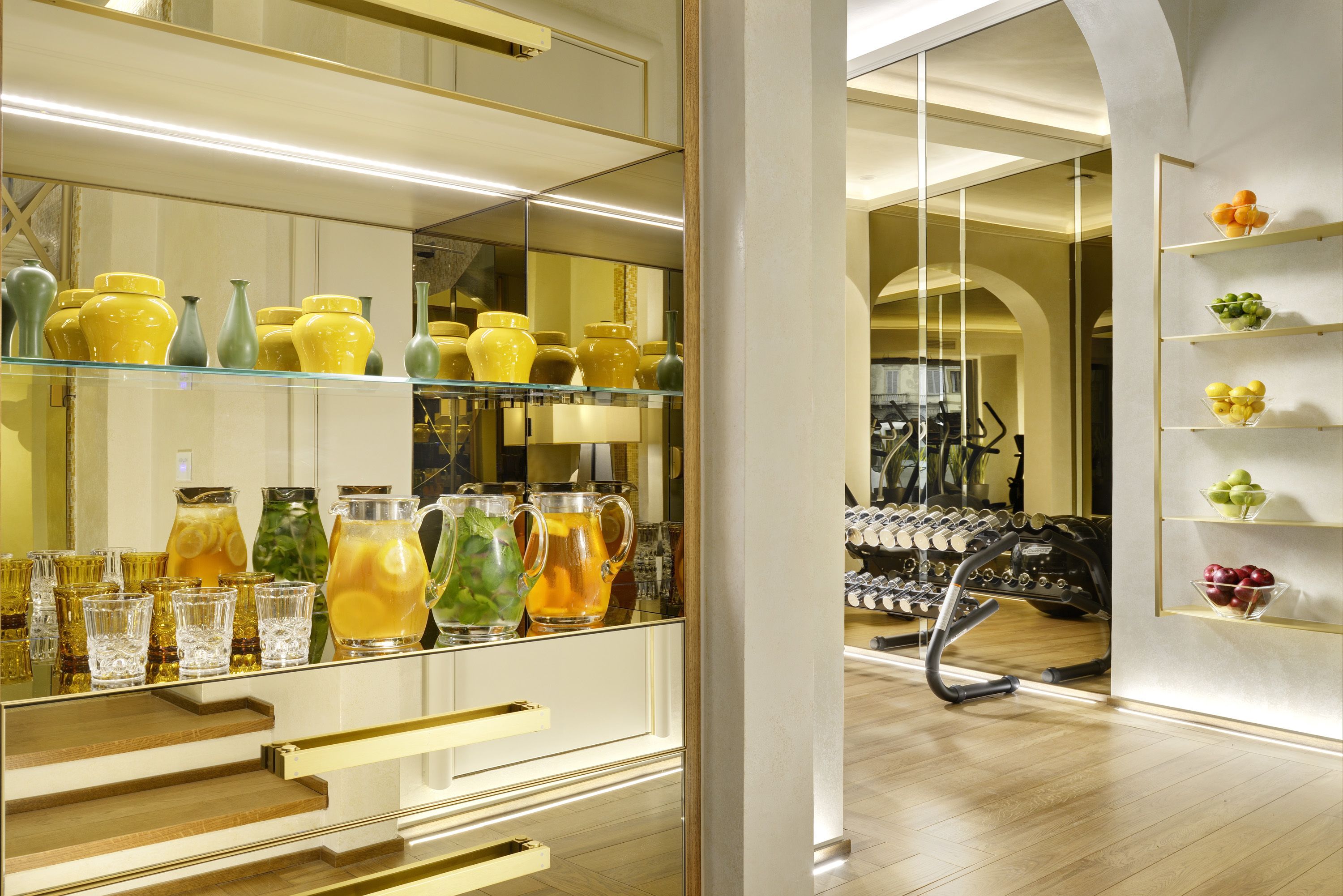 A modern interior with a glass display of yellow and green vases, a mirrored wall, and a wooden floor.