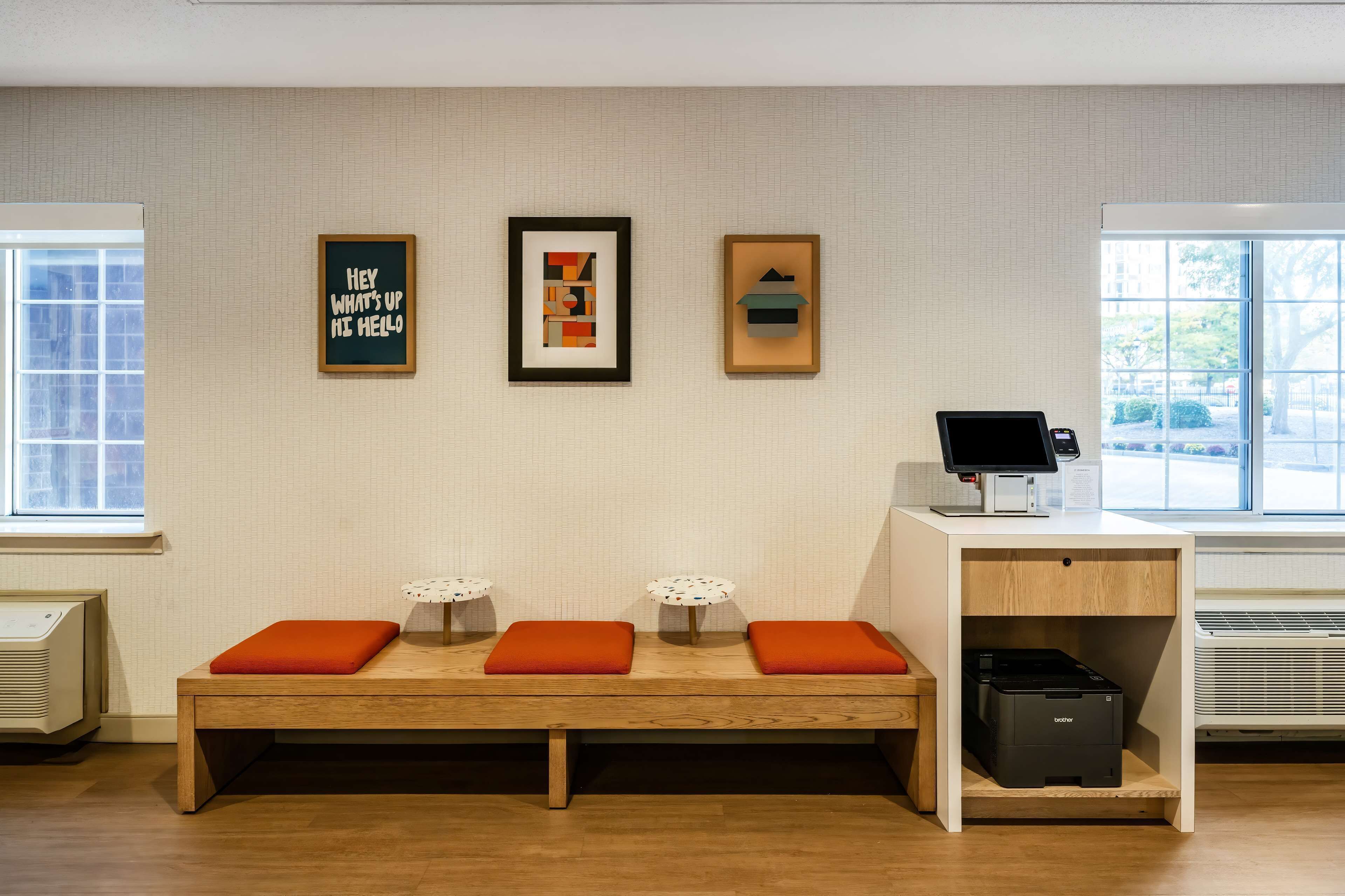 Un área de recepción con un banco de madera, tres obras de arte enmarcadas, un mostrador de recepción e impresora.