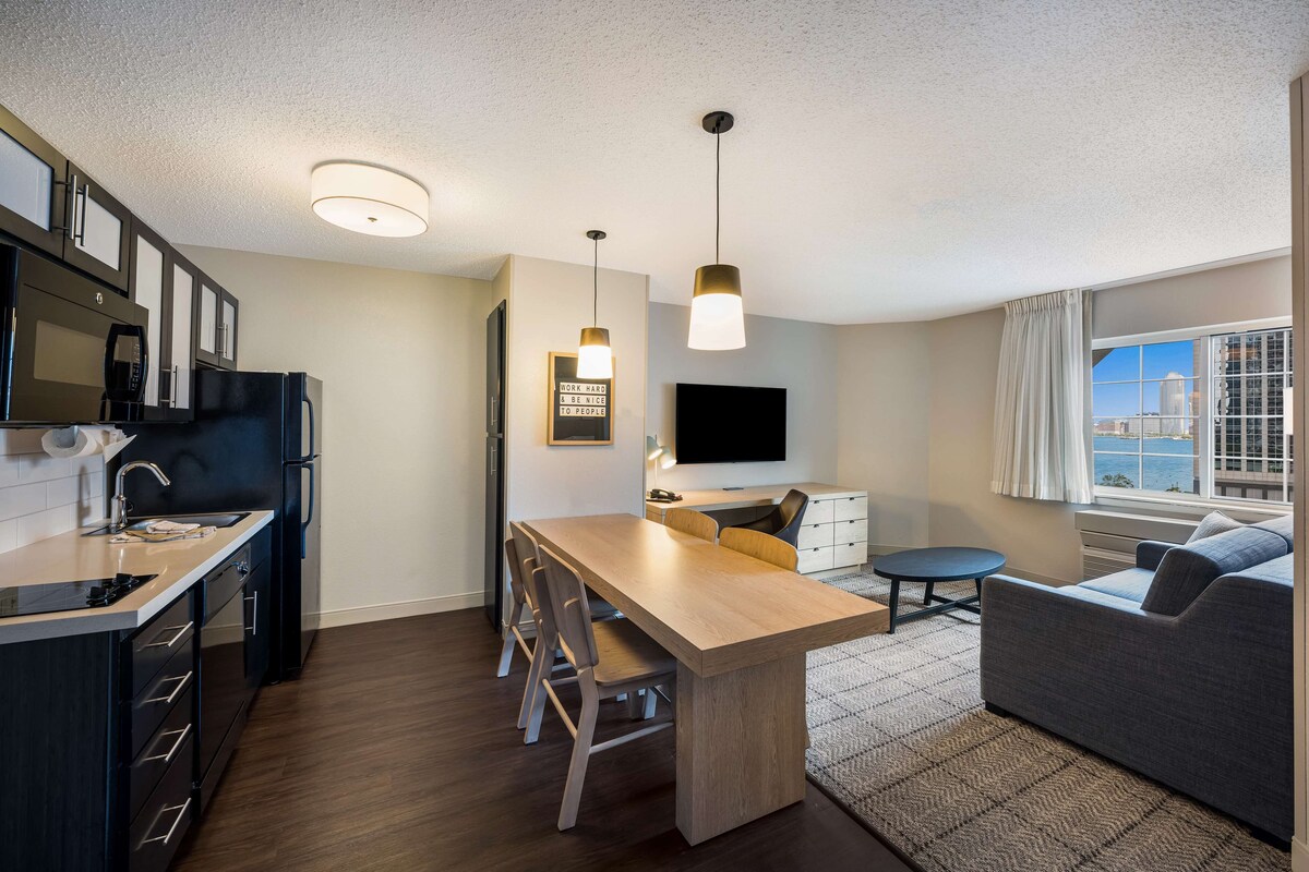 A modern kitchen with a dining area, a flat-screen TV, and a view of the city.