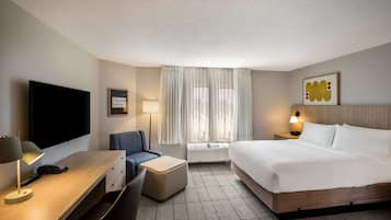 Een hotelkamer met een bed, een bureau met lamp, een stoel, een televisie en een raam met gordijnen.