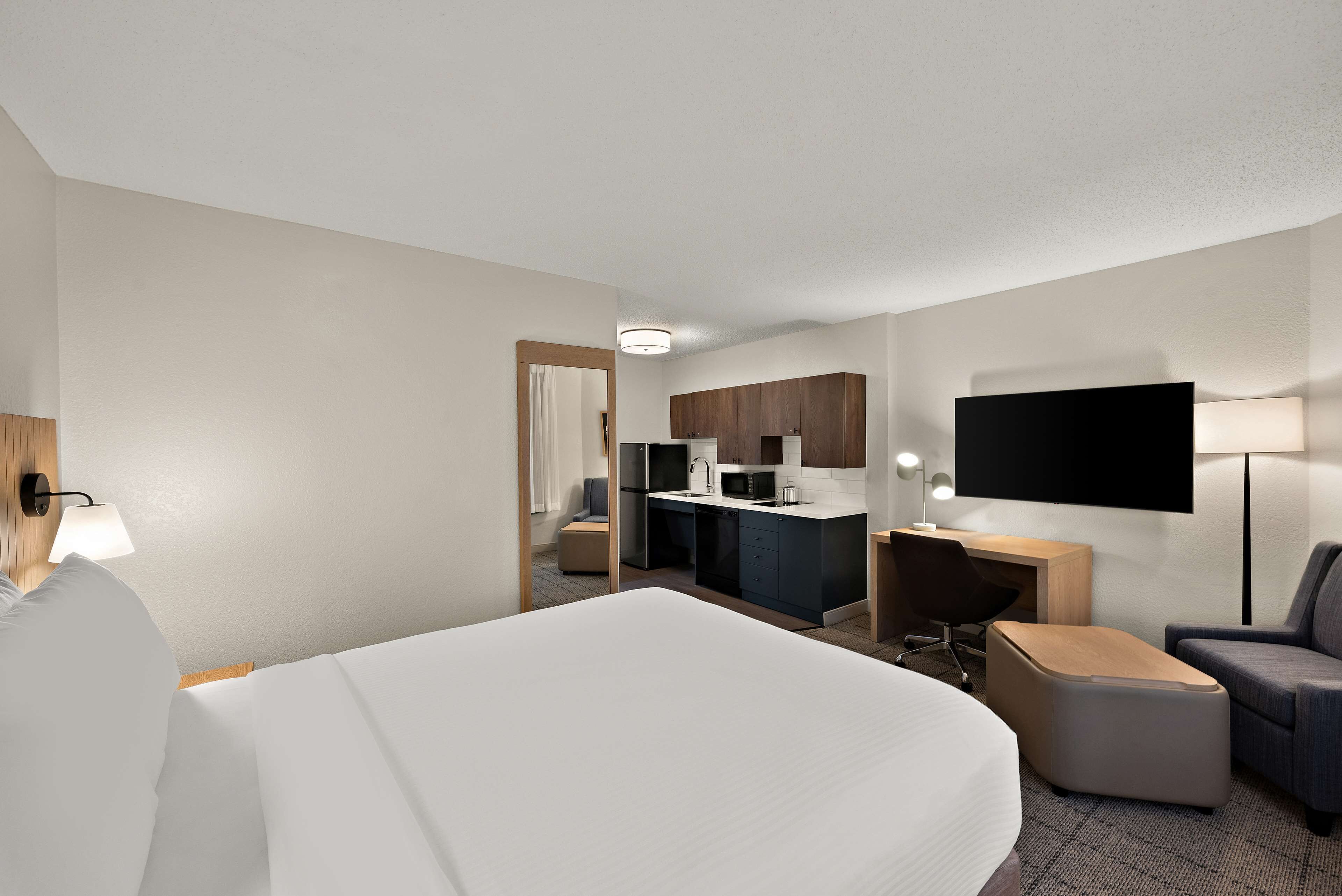 A hotel room with a bed, a desk, a chair, a TV, and a kitchenette.