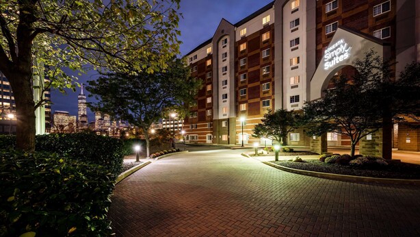 A hotel entrance with a brick pathway leading to the building, surrounded by trees and well-lit by street lamps. - Sonesta Simply Suites Jersey City (Jersey City)