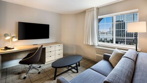 A modern hotel room with a flat-screen TV, a desk with a chair, a sofa, and a window with a city view. - Sonesta Simply Suites Jersey City (Jersey City)