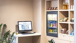 A shop area with a computer monitor displaying a website, a refrigerator stocked with beverages, and shelves with snacks. - Aparthotel Adagio Paris Haussmann (Paris)
