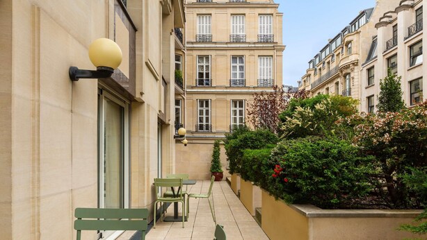 A narrow outdoor corridor with a table and chairs, a potted plant, and a building with balconies. - Aparthotel Adagio Paris Haussmann (Paris)