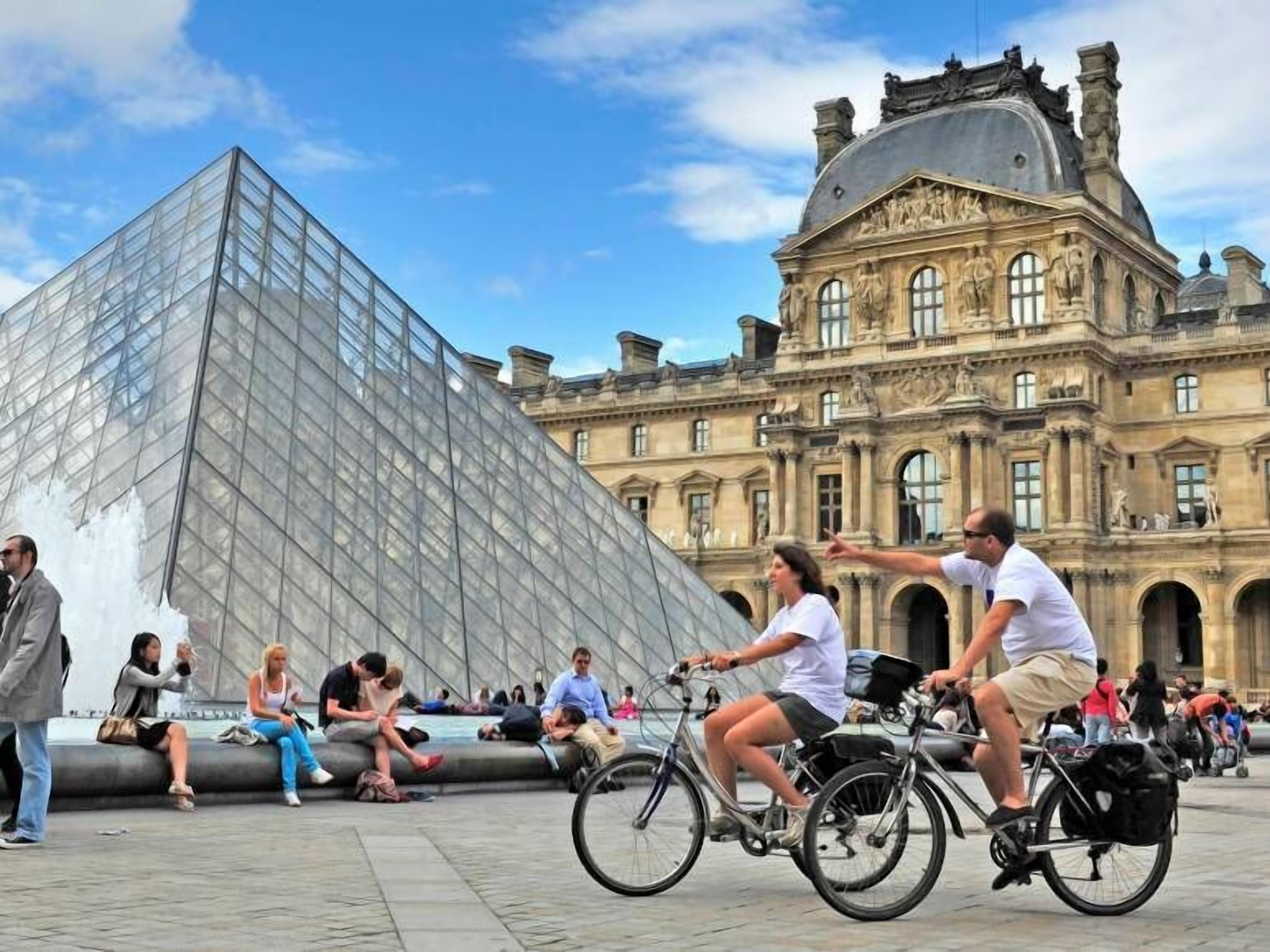 Une grande pyramide de verre et un bâtiment historique à l’architecture classique.